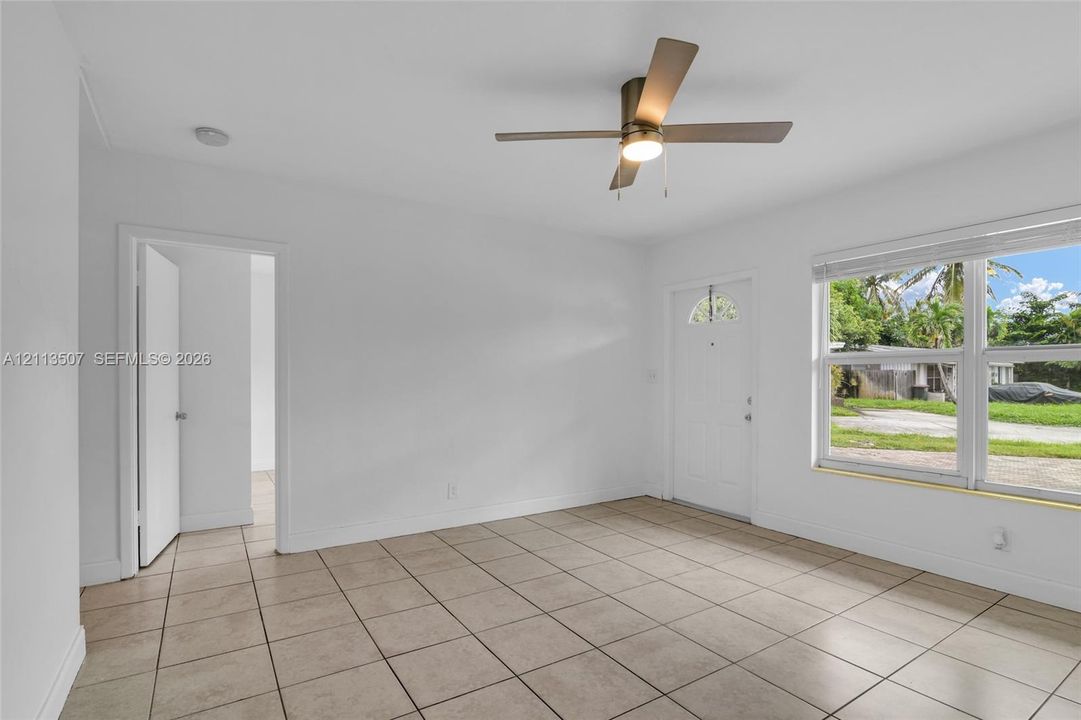 Neutral-toned tile flooring, minimalist white walls, ceiling-mounted fan with integrated lighting, and white exterior door with glass insert