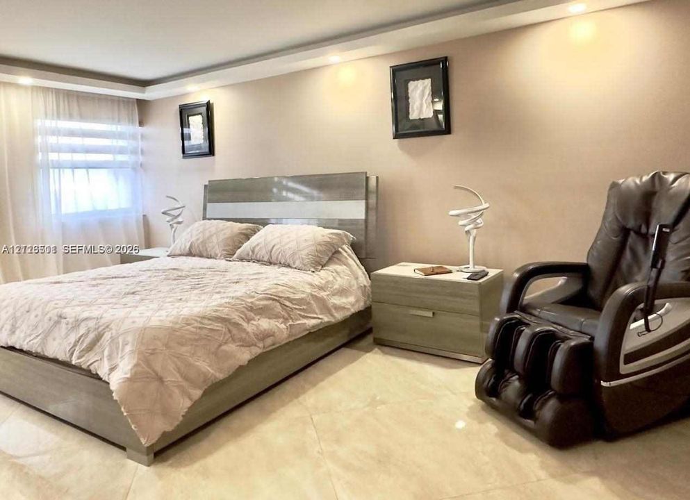 Spacious bedroom featuring recessed ceiling lighting, large-format tile flooring, and a window fitted with horizontal blinds