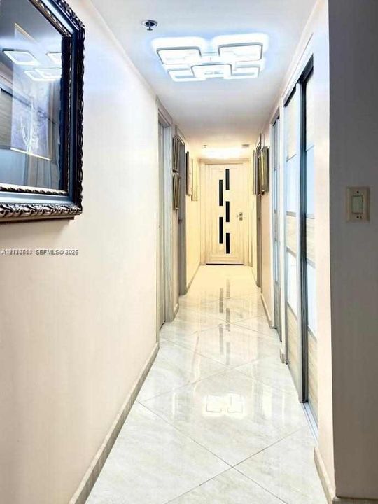 Hallway featuring high-gloss tile flooring, geometric LED ceiling light fixture, and sliding door closet with wood-finish paneling