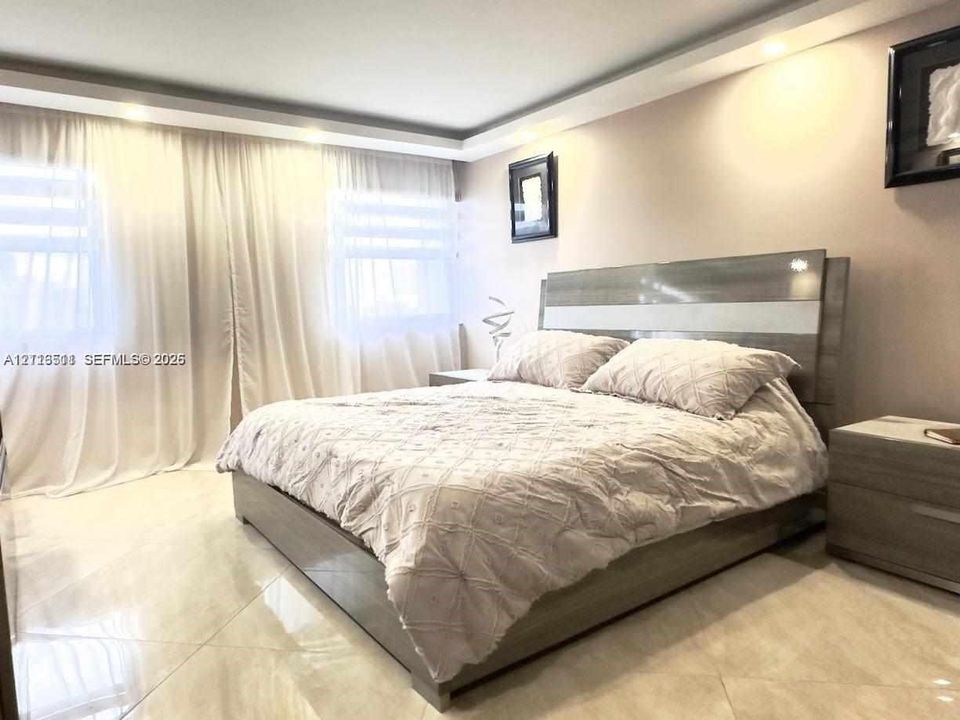 Large-format tile flooring, tray ceiling with recessed lighting, and wall-to-wall drapery