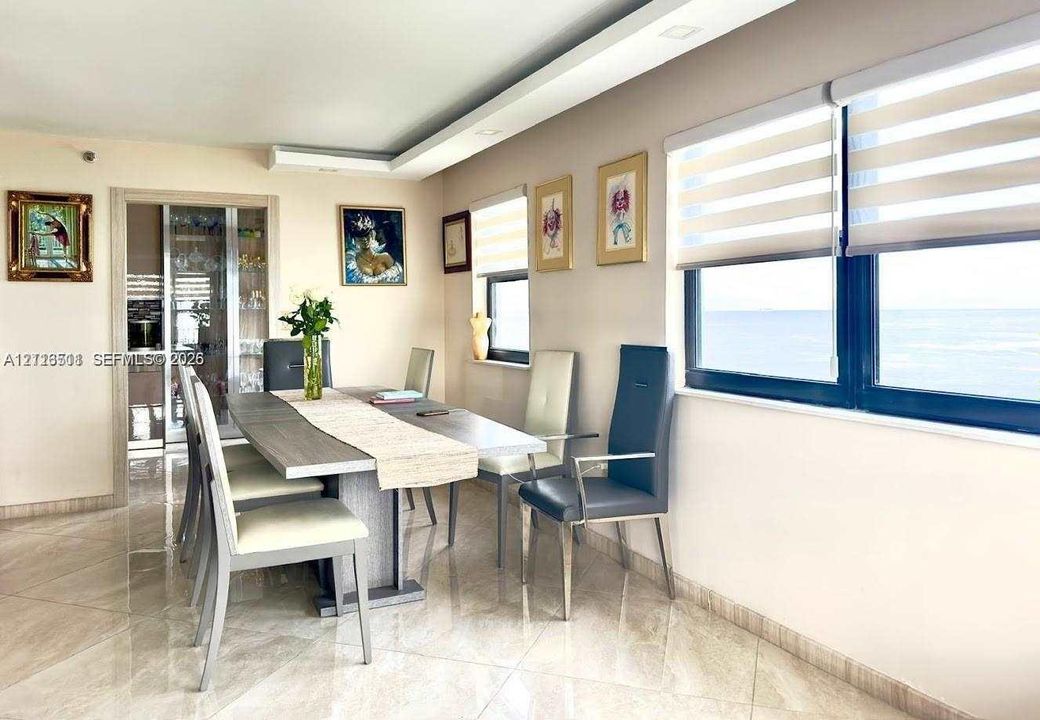 Large format tile flooring, tray ceiling with recessed lighting, built-in display cabinetry, and oversized windows with layered roller shades