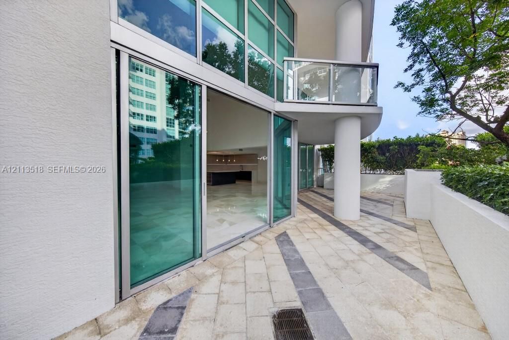 Expansive stone-paved terrace with contrasting linear accents, floor-to-ceiling glass sliding doors, elevated glass-paneled balcony, and structural concrete columns
