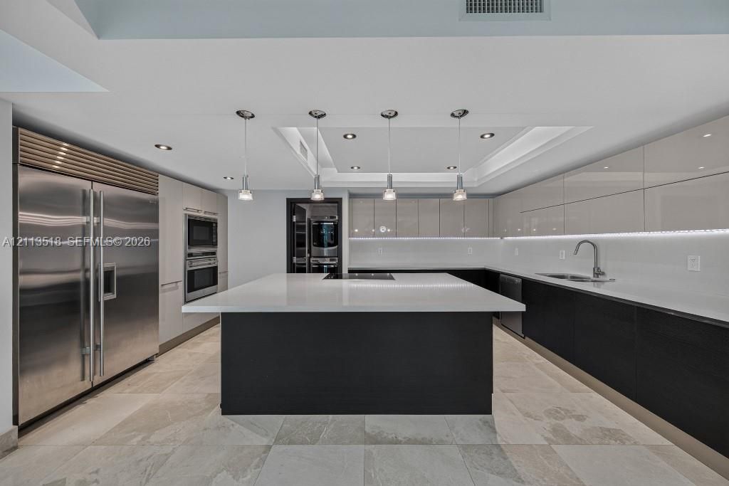 Modern kitchen featuring a central island with a stone countertop, high-gloss cabinetry, stainless steel refrigerator, recessed ceiling lighting, and tile flooring