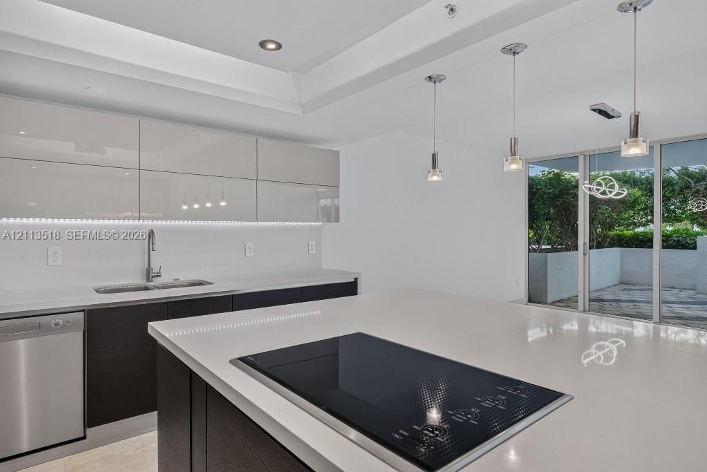 Kitchen featuring high-gloss cabinetry, stone countertops, a stainless steel dishwasher, a built-in cooktop, and recessed tray ceiling lighting