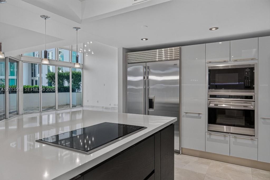 Kitchen featuring high-gloss cabinetry, a large central island with an integrated cooktop, stainless steel professional-grade appliances, recessed lighting, and floor-to-ceiling windows