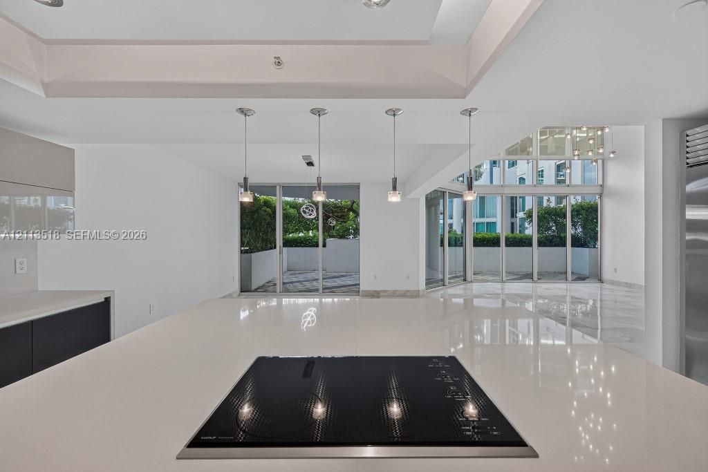 Kitchen island featuring a solid surface countertop, built-in induction cooktop, four pendant light fixtures, and multi-panel floor-to-ceiling glass sliding doors