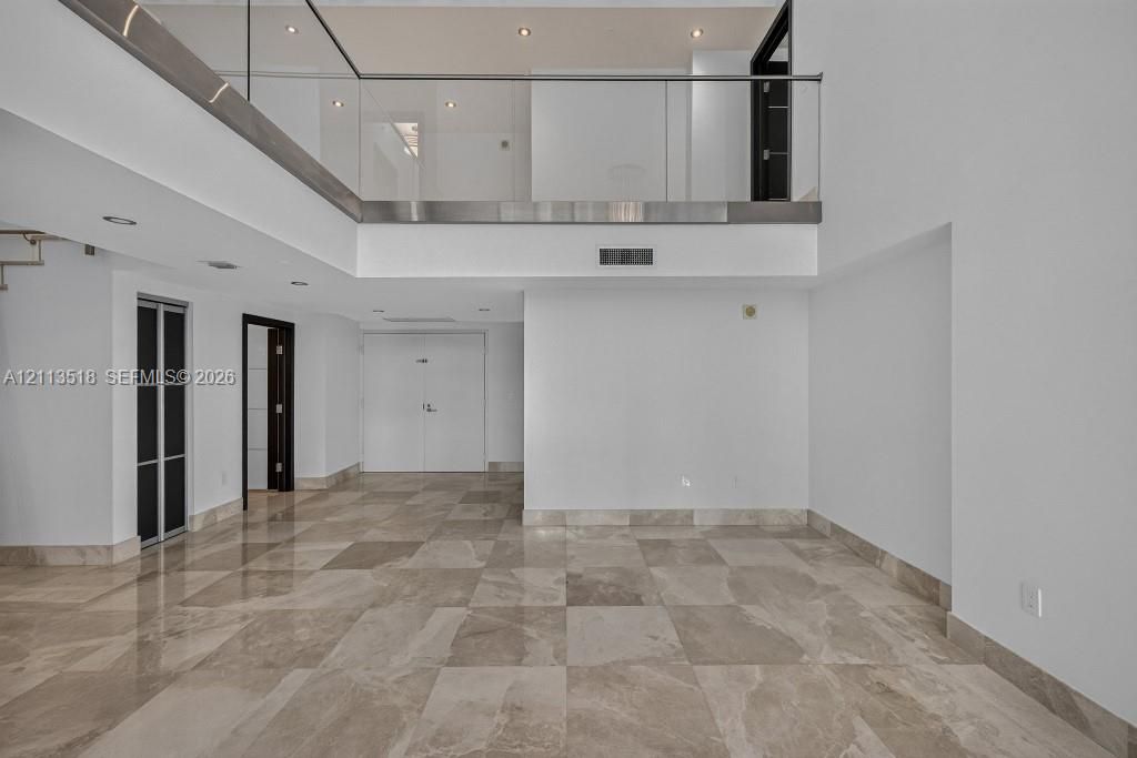 Interior space featuring high ceilings, polished stone flooring, a glass-panel mezzanine railing, recessed lighting, and multi-panel doors