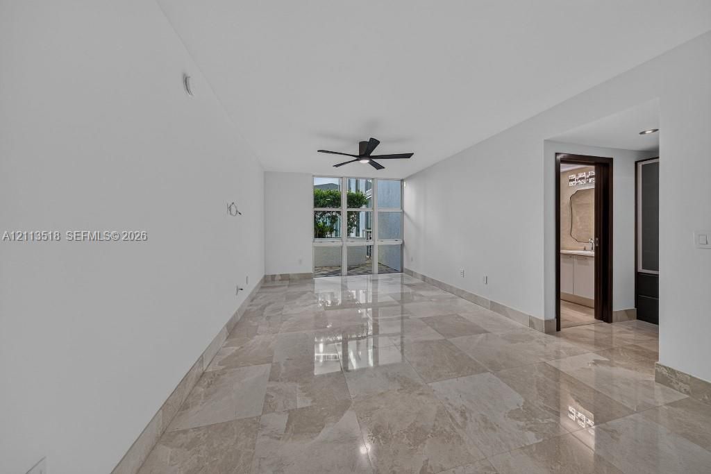Interior space featuring polished natural stone flooring, floor-to-ceiling windows, and a matte black ceiling fan