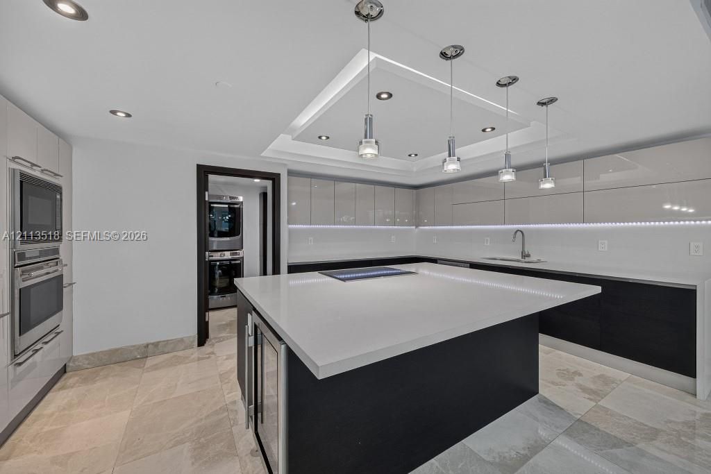 Kitchen featuring high-gloss cabinetry, a central island with a solid-surface countertop, recessed tray ceiling lighting, stainless steel built-in appliances, and tile flooring