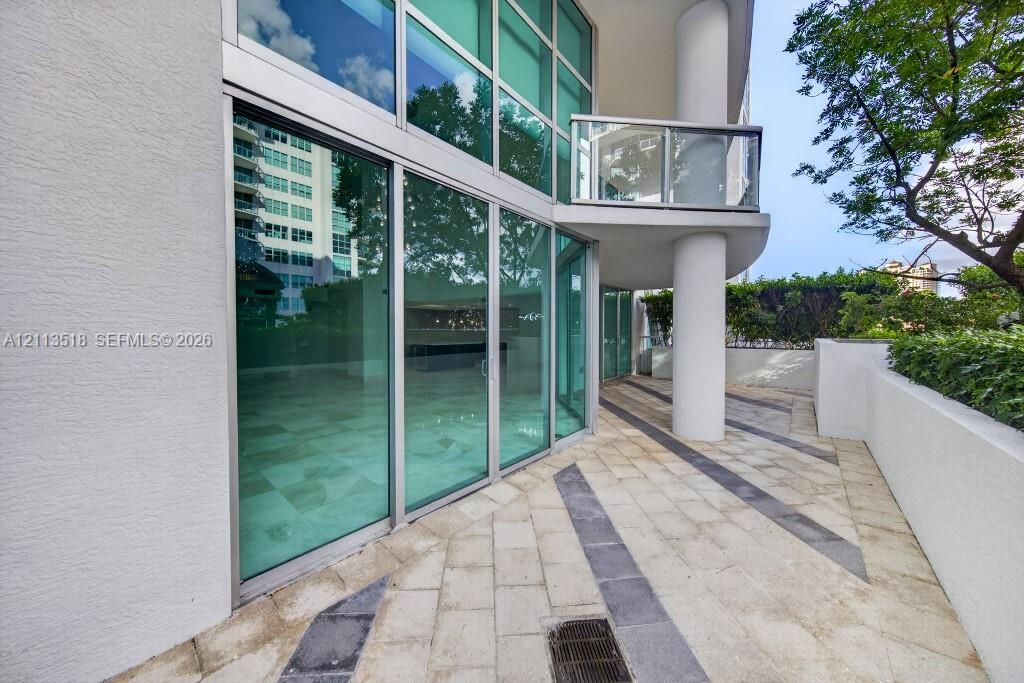 Outdoor terrace featuring floor-to-ceiling glass paneling, geometric stone paver inlay, concrete structural column, and glass-railing balcony