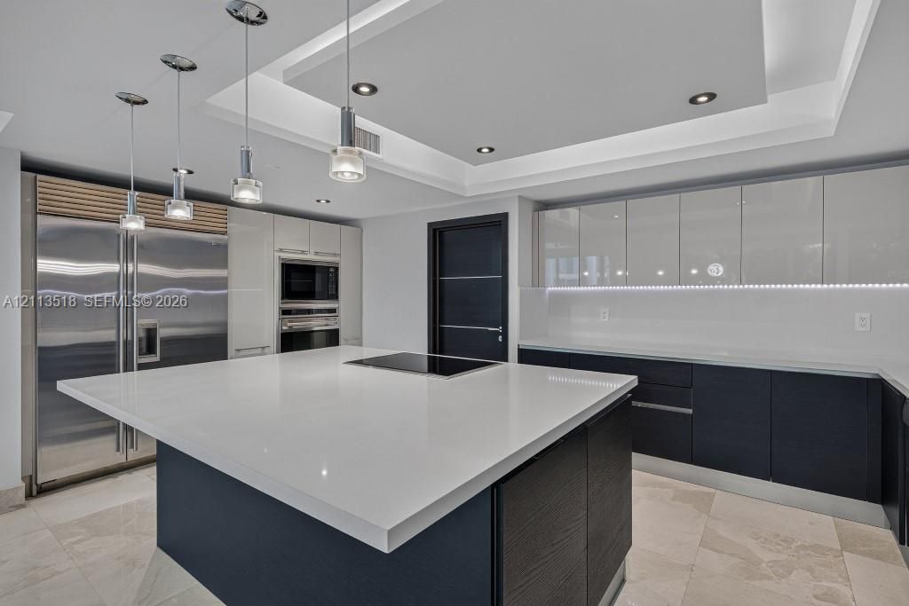 Contemporary kitchen featuring a spacious center island with a stone countertop, high-gloss cabinetry, stainless steel professional-grade appliances, recessed ceiling lighting, and tile flooring