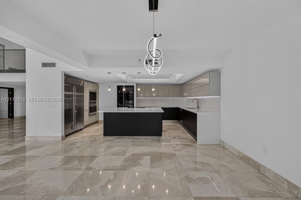 Kitchen featuring high-gloss cabinetry, stone countertops, central island, integrated stainless steel appliances, and large-format tile flooring