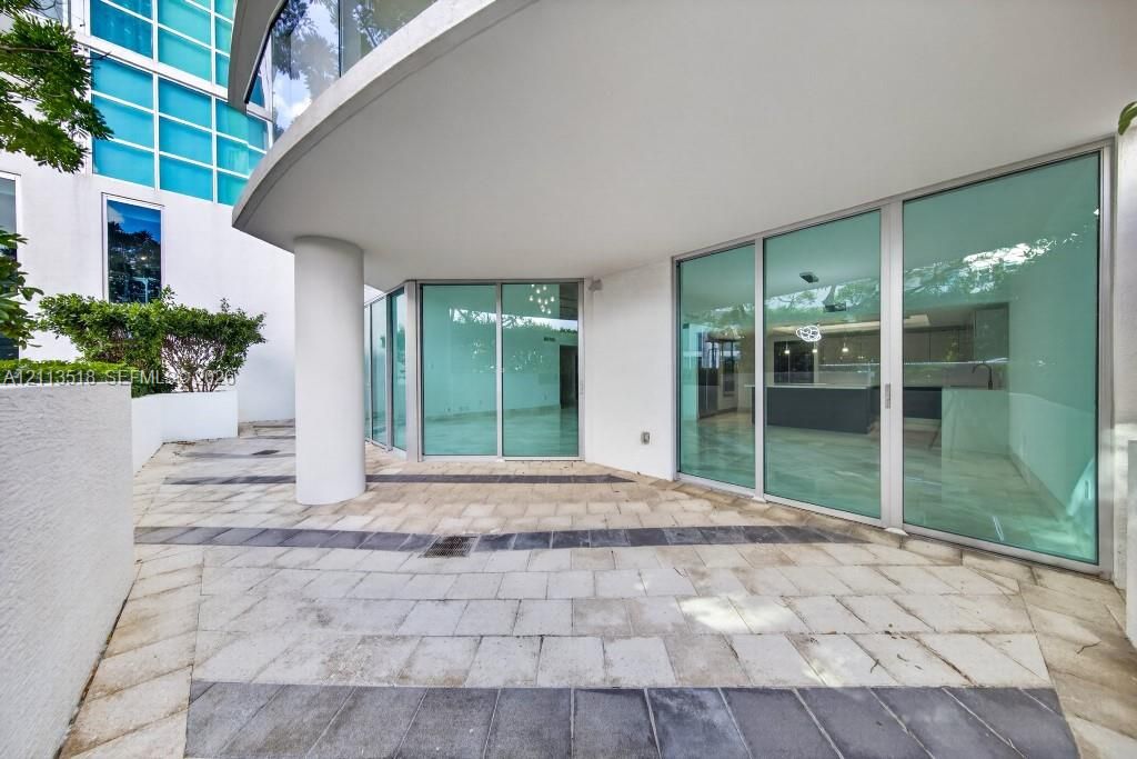 Curved stone patio featuring decorative inlaid tile patterns, expansive floor-to-ceiling glass walls, and a structural concrete support column