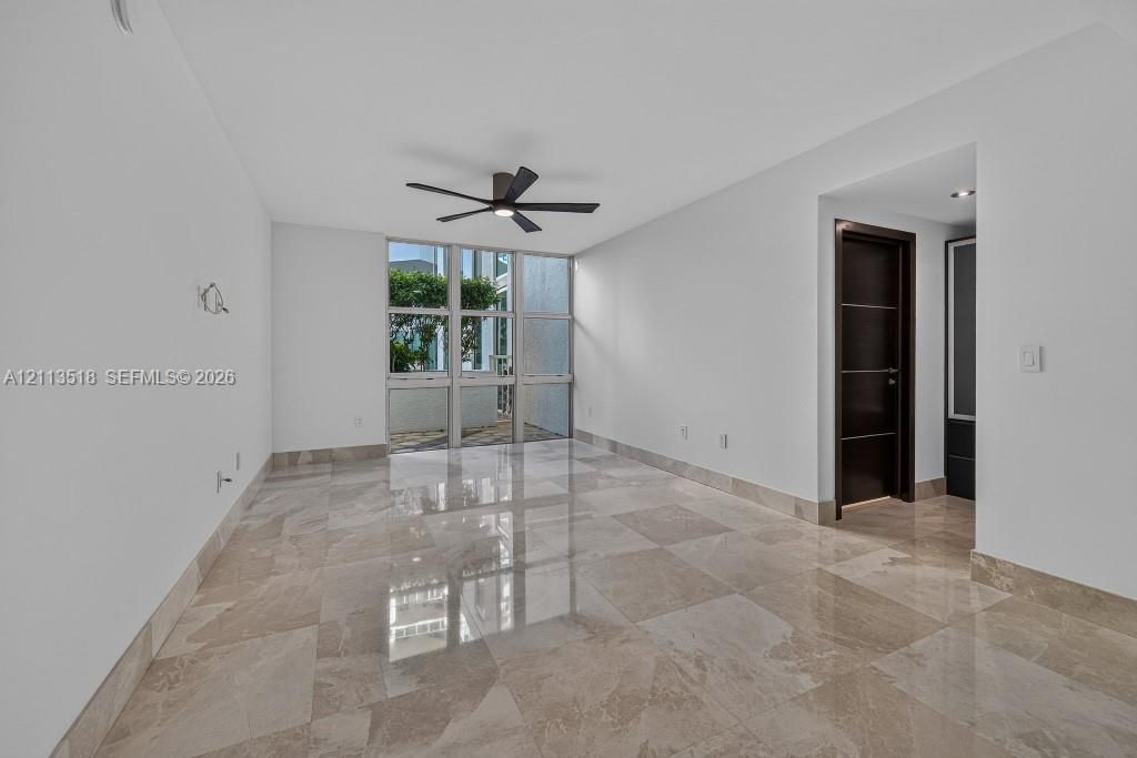 Interior space featuring large-format stone tile flooring, floor-to-ceiling windows, and a matte black ceiling fan