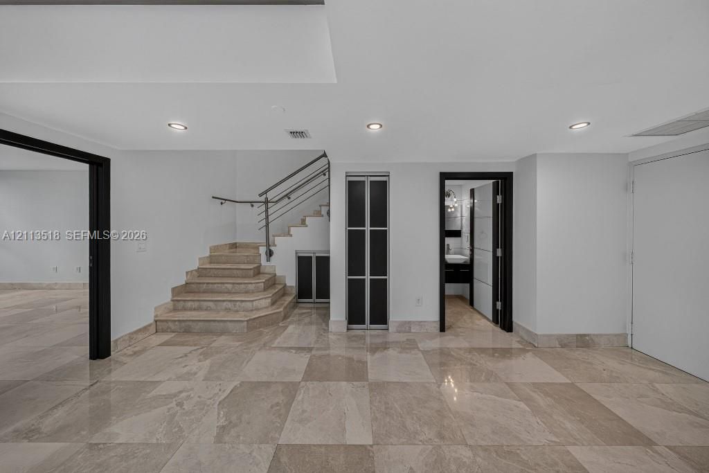 Polished stone flooring, recessed lighting, staircase with metal railings, and contrasting dark-framed doorways