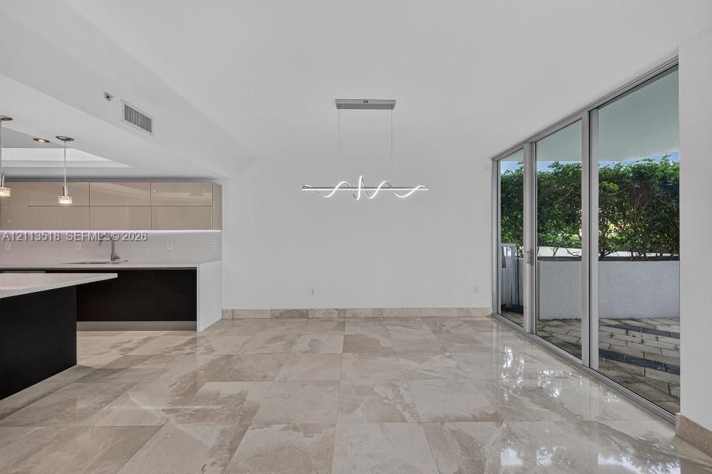 Open-concept interior featuring large-format tile flooring, high-gloss cabinetry, a quartz waterfall island, modern linear architectural lighting, and floor-to-ceiling glass sliding doors