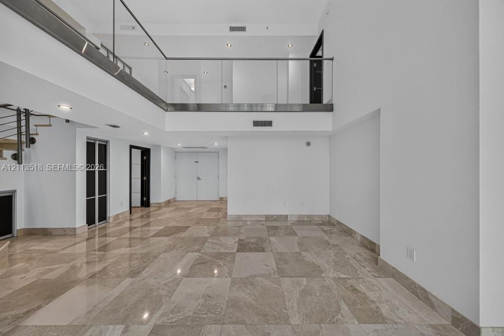 Double-height ceilings with an open mezzanine, glass railing, stone flooring, and recessed lighting