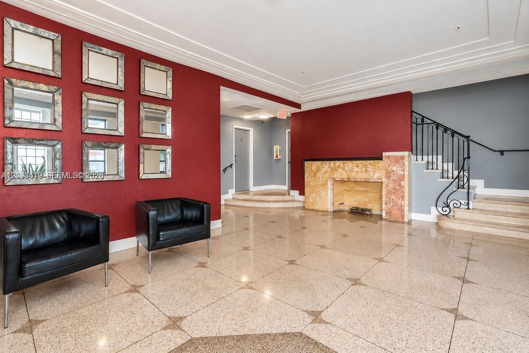 Foyer featuring polished stone flooring with geometric inlays, a stone-clad fireplace surround, a decorative iron staircase railing, crown molding, and a grid of wall-mounted mirrors