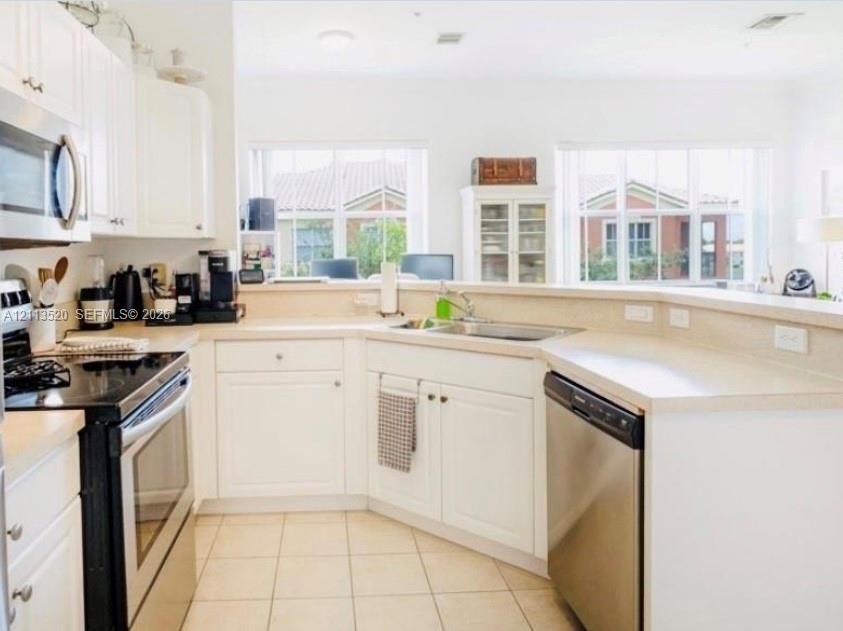 Kitchen featuring white cabinetry, solid surface countertops, stainless steel appliances, ceramic tile flooring, and windows with pane detailing