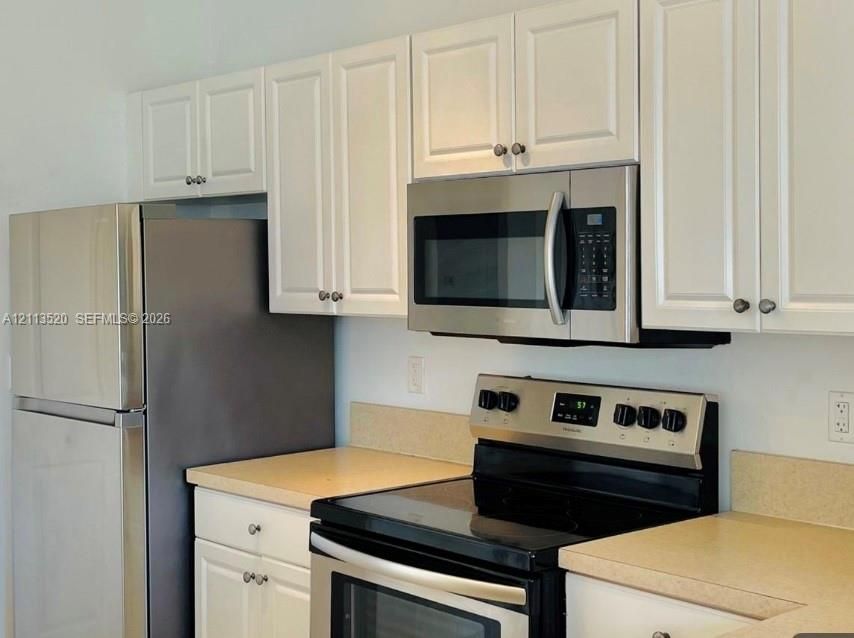 Kitchen featuring white shaker-style cabinetry, stainless steel refrigerator, over-the-range stainless steel microwave, and solid-surface countertops