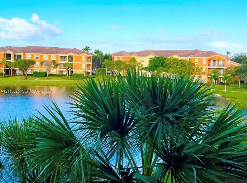 Multi-story structures with tile roofs and private balconies overlooking a lake, featuring mature palms and landscaped grounds