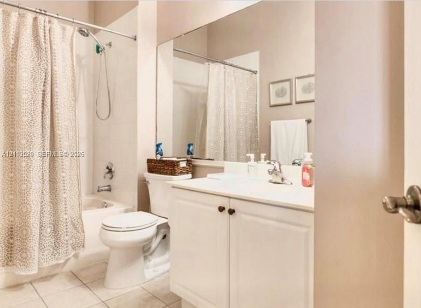 Bathroom featuring a vanity with white cabinetry and a solid-surface countertop, full-width wall mirror, tile flooring, and a shower-tub combination with chrome fixtures