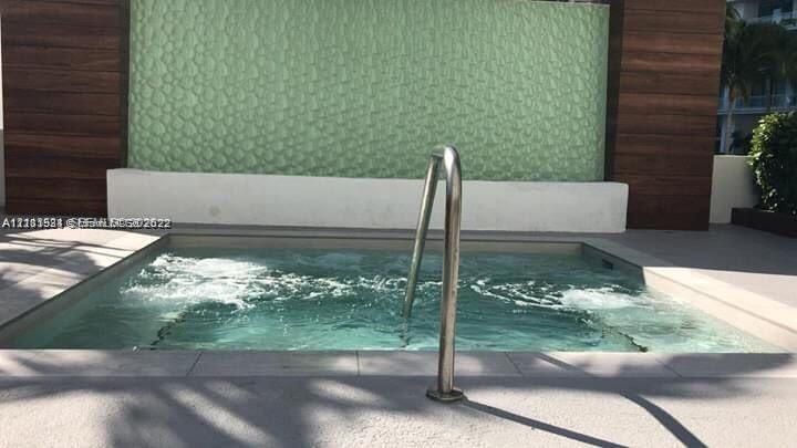 In-ground spa featuring a textured water feature wall, wood-finish paneling, and a stainless steel grab rail