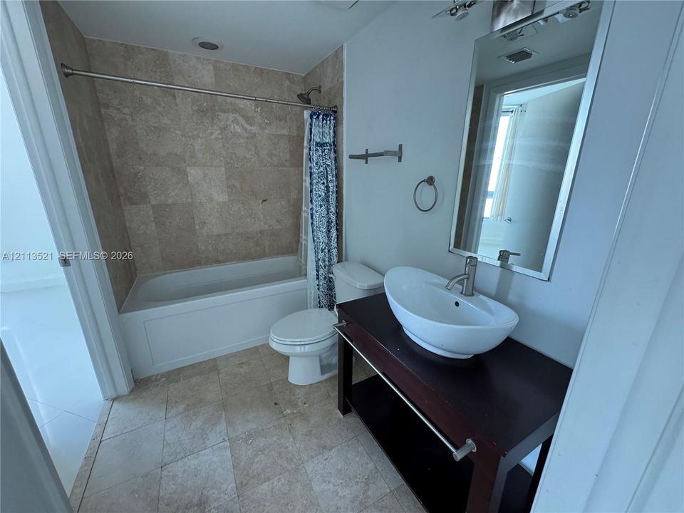 Bathroom featuring a dark wood-finish vanity with a white vessel sink, brushed nickel hardware, wall-mounted rectangular mirror, and a tub with tiled surround