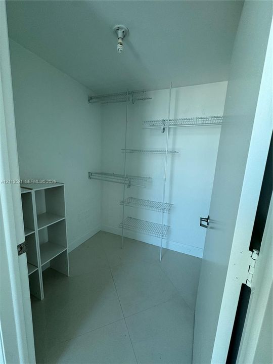 Walk-in storage space featuring ceramic tile flooring, built-in wire shelving, and an additional freestanding open-shelf unit