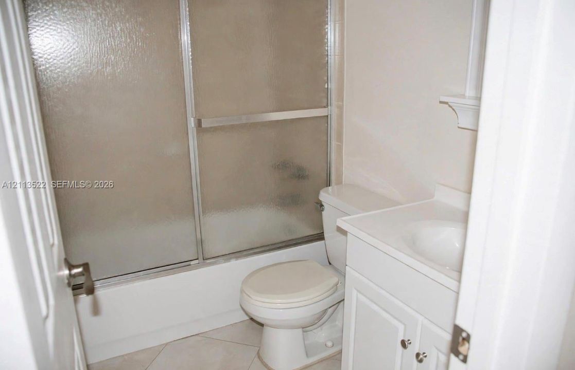 Bathroom featuring white cabinetry, integrated sink, tub-shower combination with sliding glass doors, and light-toned tile flooring