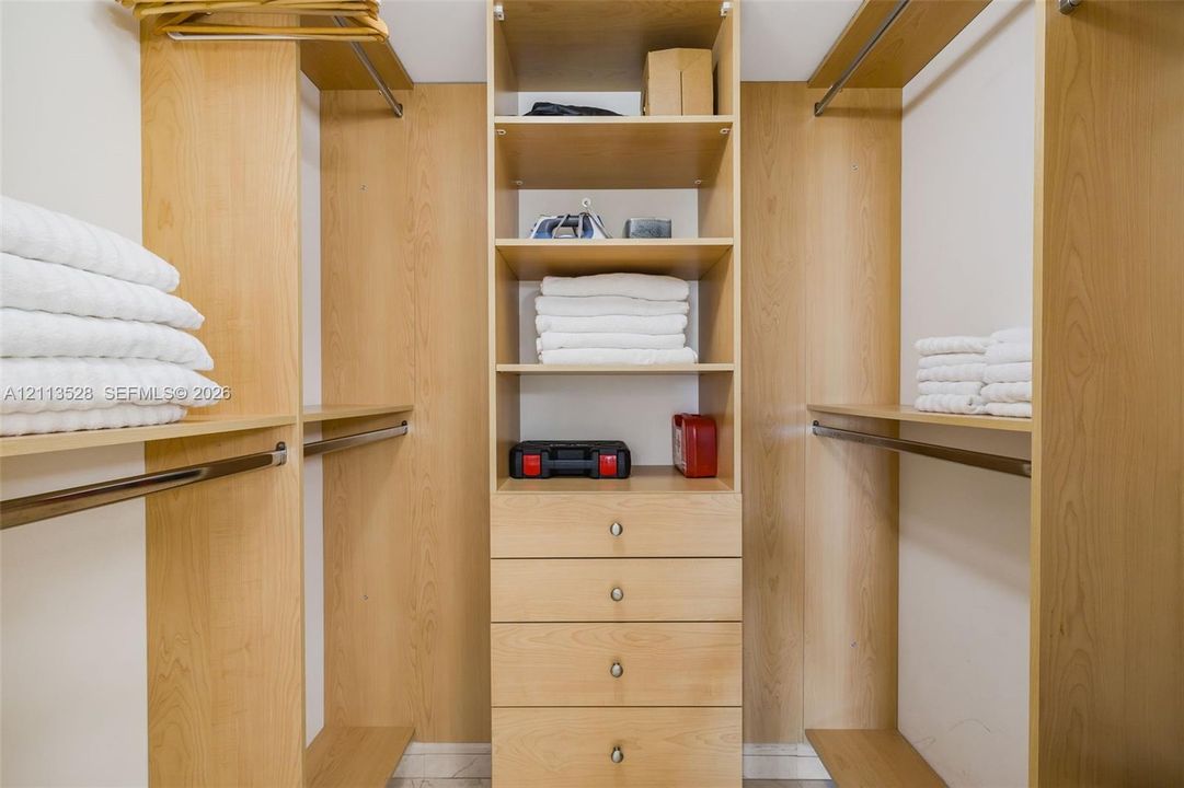 Customized closet organization system featuring light wood-finish shelving, integrated hanging rods, and a center stack of four built-in drawers