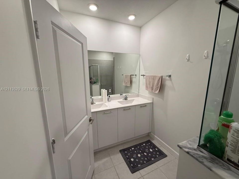 Bathroom featuring a double-sink vanity with white cabinetry and a solid-surface countertop, full-width wall mirror, recessed lighting, and tile flooring