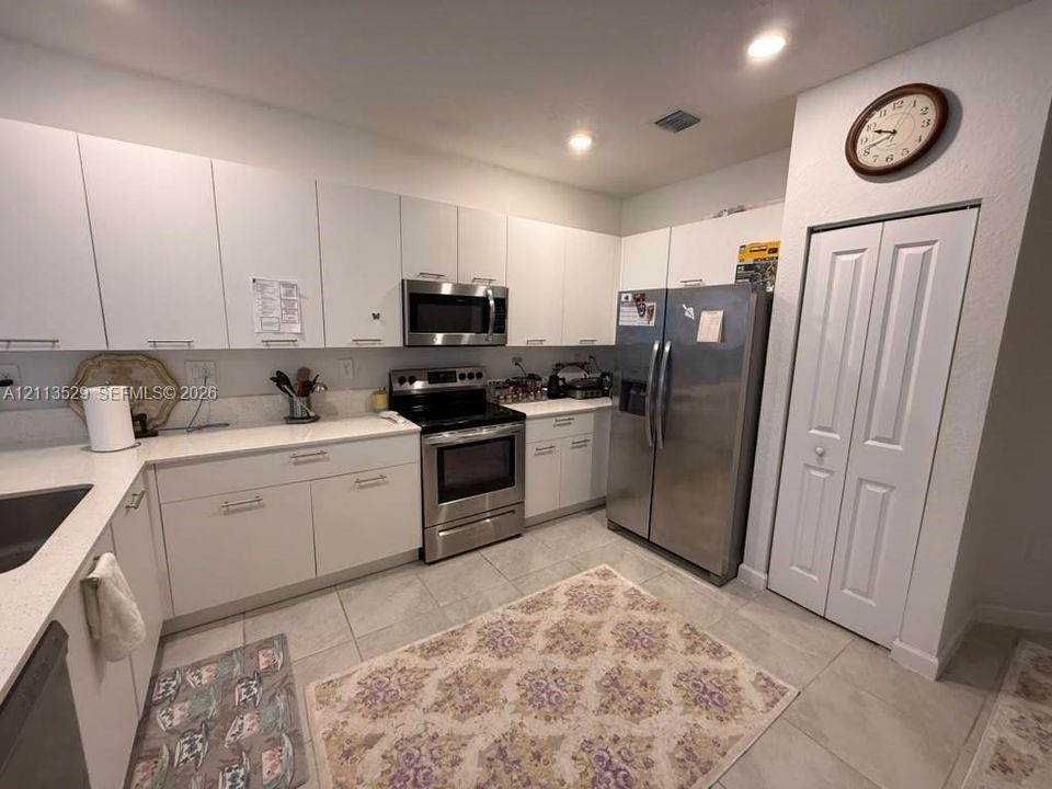 Kitchen featuring flat-panel white cabinetry, light-toned stone-finish countertops, stainless steel appliances, tile flooring, and a floor-to-ceiling built-in pantry with bi-fold doors