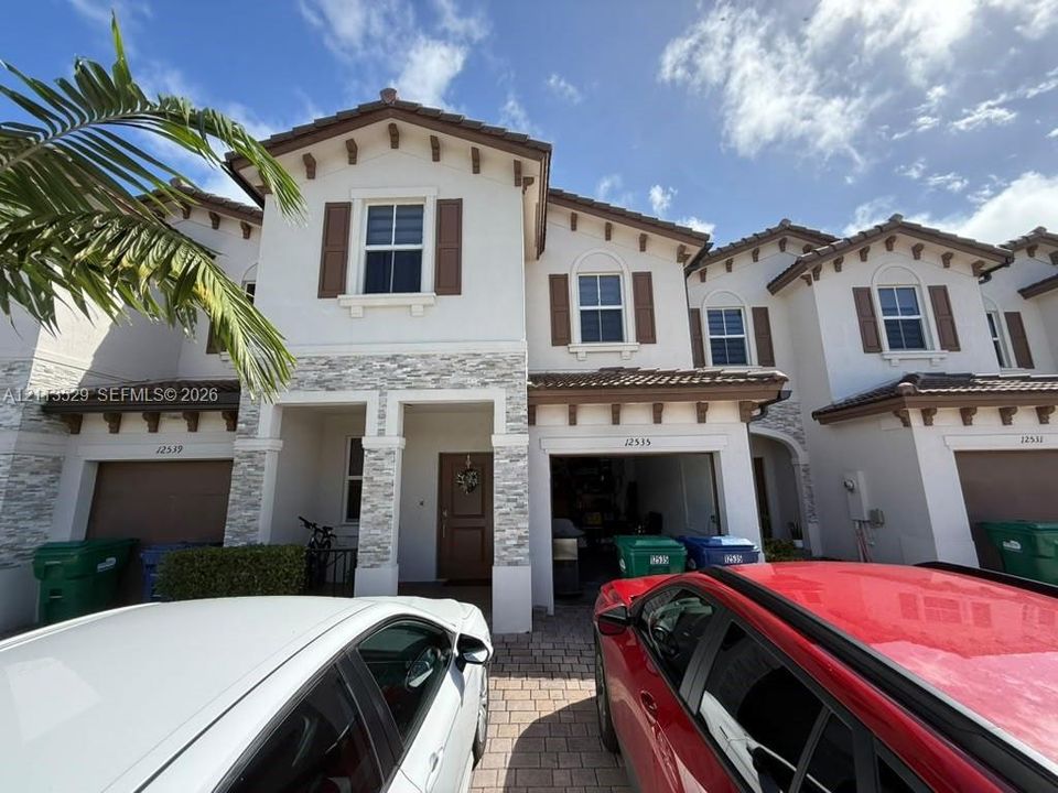 Stucco exterior featuring stacked stone accents, decorative corbels, paver driveway, and arched window detailing