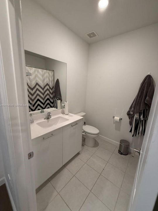 Bathroom featuring a white vanity cabinet with a stone-composite countertop, an integrated rectangular sink, large-format neutral floor tile, and a wall-mounted mirror