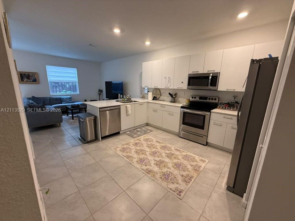 Kitchen featuring flat-panel white cabinetry, stainless steel appliances, solid-surface countertops, recessed lighting, and tile flooring