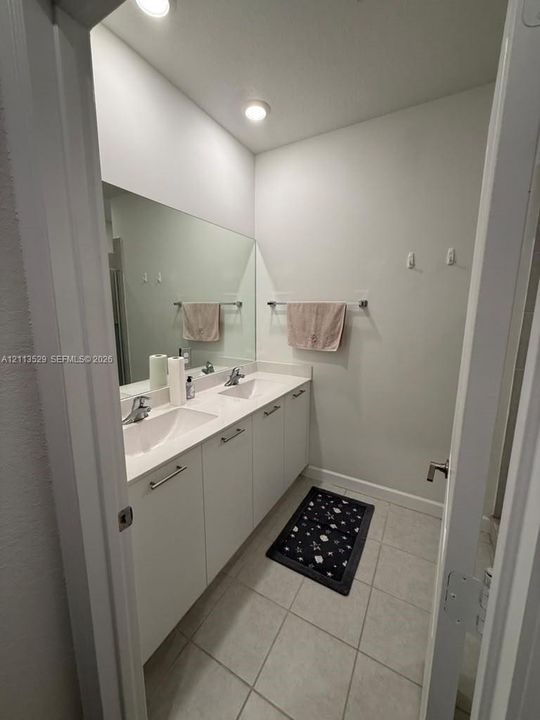 Dual-sink vanity with white cabinetry, light-toned countertop, integrated rectangular basins, polished chrome faucets, and a full-width wall mirror