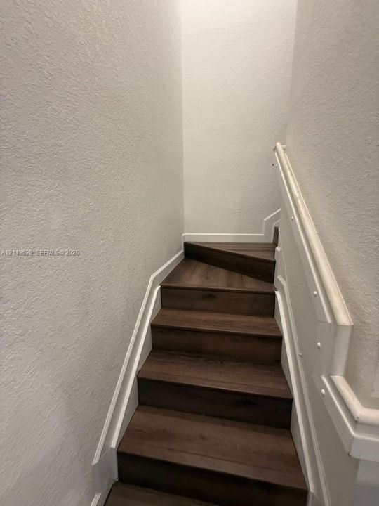 Staircase featuring wood-finish treads, white paneled walls, and a matching white handrail