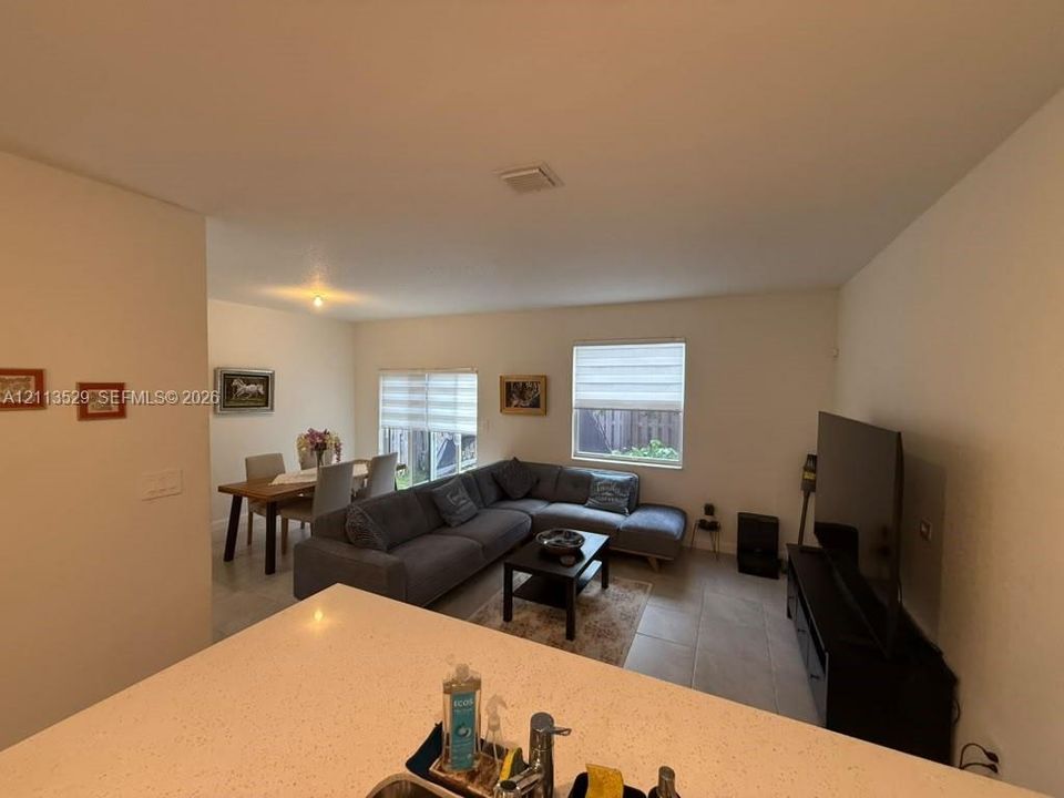 Open-concept interior featuring light-toned tile flooring, neutral wall paint, tiered window shades, and a countertop with an integrated stainless steel sink