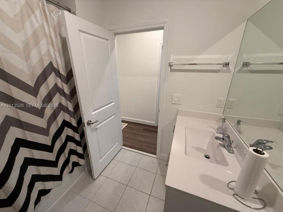 Bathroom featuring a vanity with a white solid-surface countertop, integrated rectangular sink, chrome faucet, wall-spanning mirror, and tile flooring