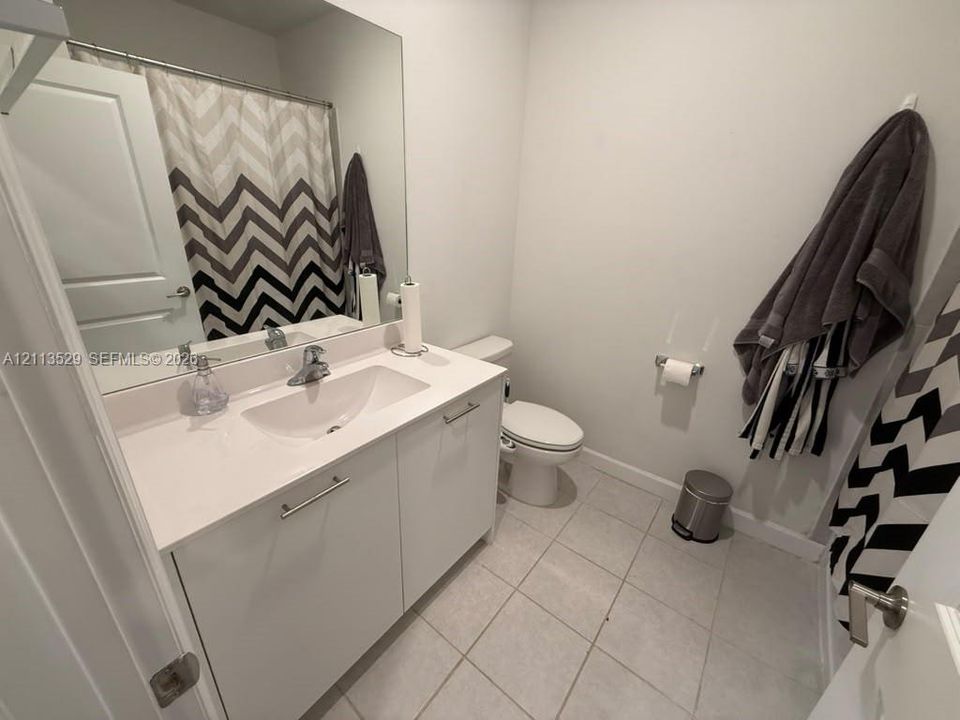 Bathroom featuring a white vanity cabinet with a solid surface countertop, an integrated basin, a full-width wall mirror, and neutral floor tile