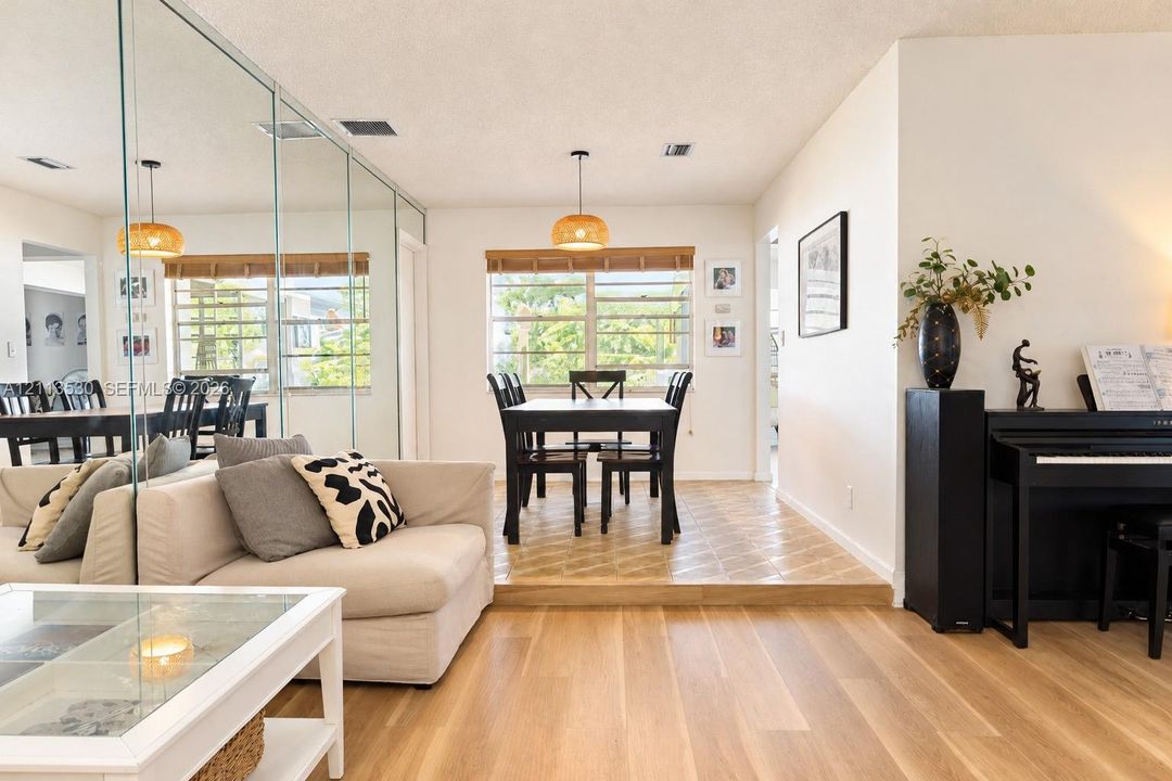 Sunlit room featuring wood-finish flooring, a wall-to-wall mirrored accent, tiered floor elevation, and dual pendant light fixtures
