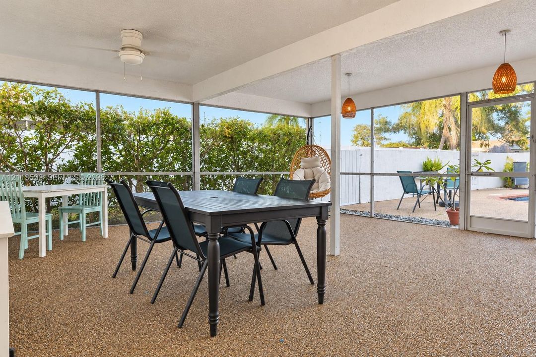 Screened-in patio featuring textured aggregate flooring, dual pendant lighting, a ceiling fan, and a glass-paneled entry door