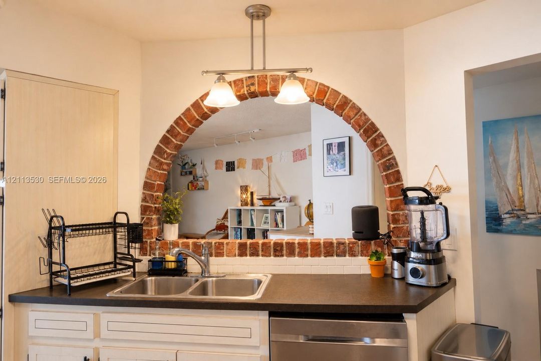 Kitchen sink area featuring an arched brick surround, stainless steel dual-basin sink, high-arc faucet, and a two-light pendant fixture