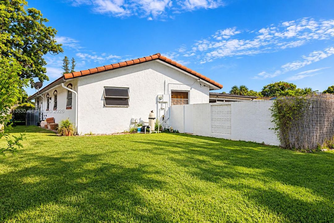 Stucco exterior with a terra cotta tile roof, expansive lawn, and a white privacy wall