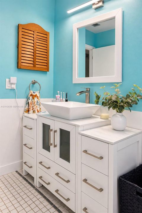 White vanity featuring a rectangular vessel sink, stone-finish countertop, cabinet doors with glass insets, and brushed metal hardware