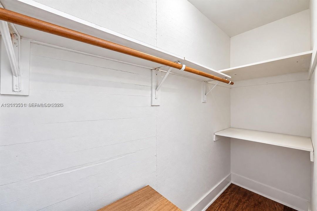 Storage area featuring white built-in shelving, a wood-finish hanging rod, and wood-finish flooring