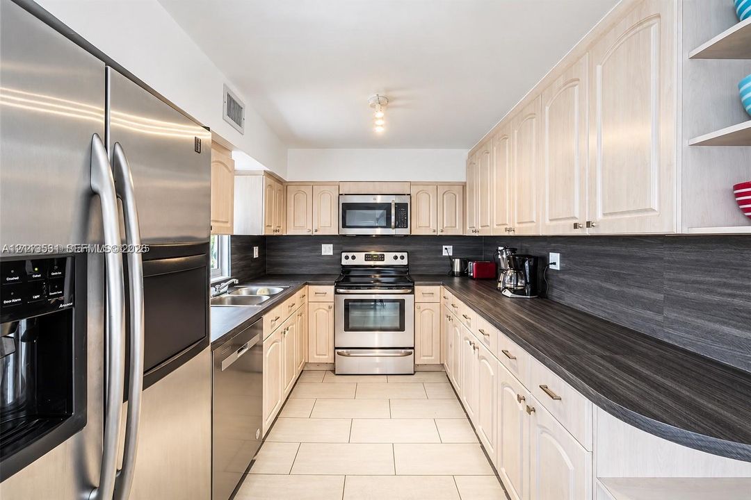 Kitchen featuring light-finish cabinetry, dark solid-surface countertops, stainless steel appliances, and tile flooring