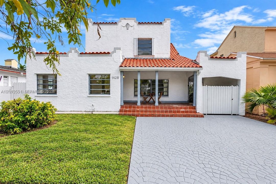 Spanish Colonial exterior featuring a white textured stucco facade, red tile roof, covered front porch with a tiered brick entryway, and decorative parapets