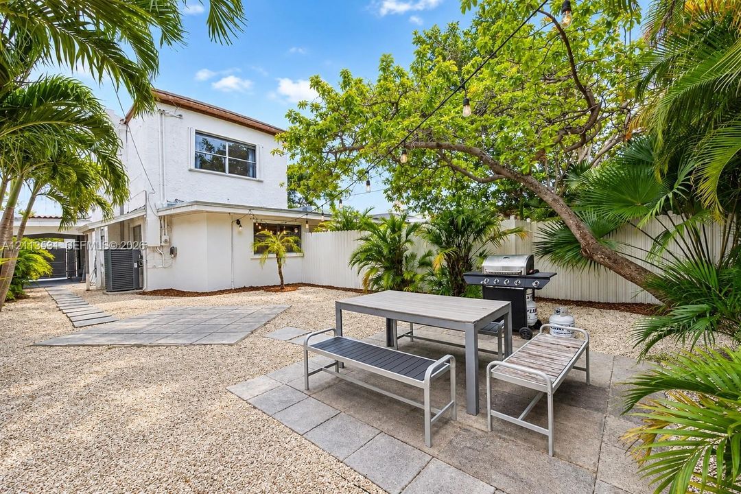 Outdoor space featuring a gravel courtyard, paver patio sections, white privacy fencing, and mature palm trees